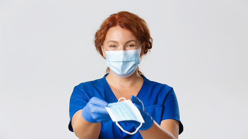 Nurse wearing and holding a surgical mask