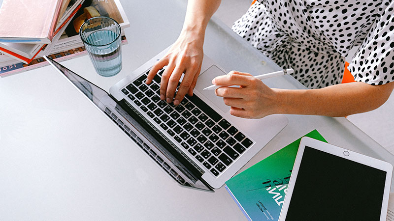 Person holding  a pencil typing on laptop computer 