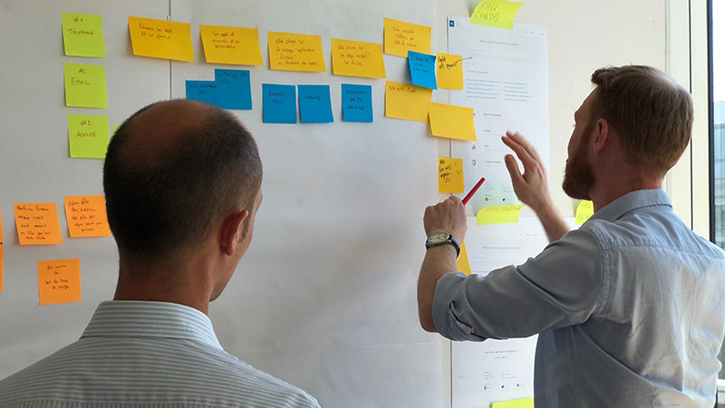 customer-experience-council Two men putting sticky notes on wall