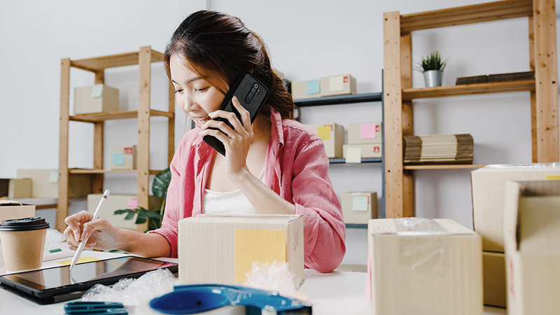 Woman of phone with package boxes and packing tape around her